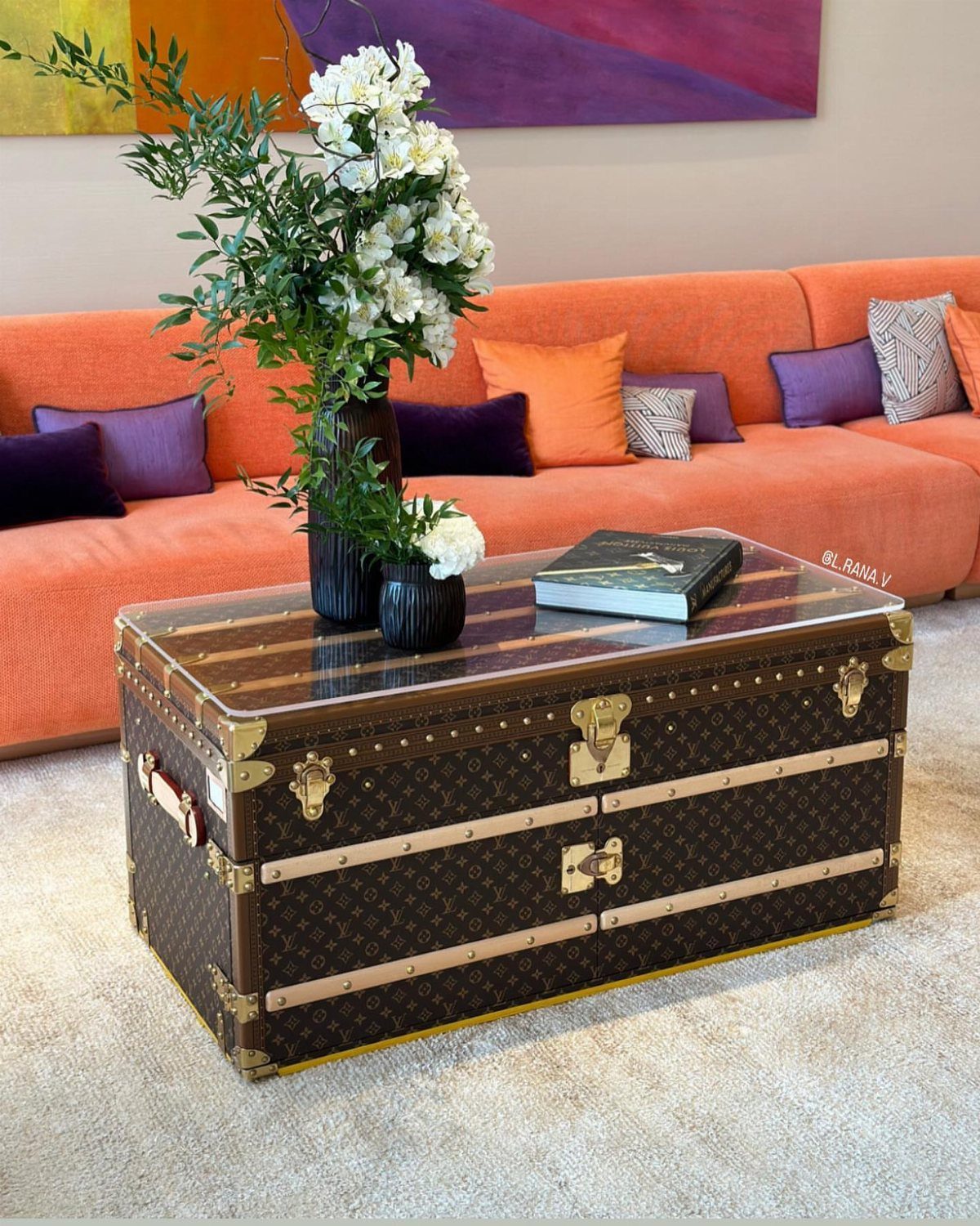 Brown patterned vintage trunk coffee table with glass top and white flowers in vases.