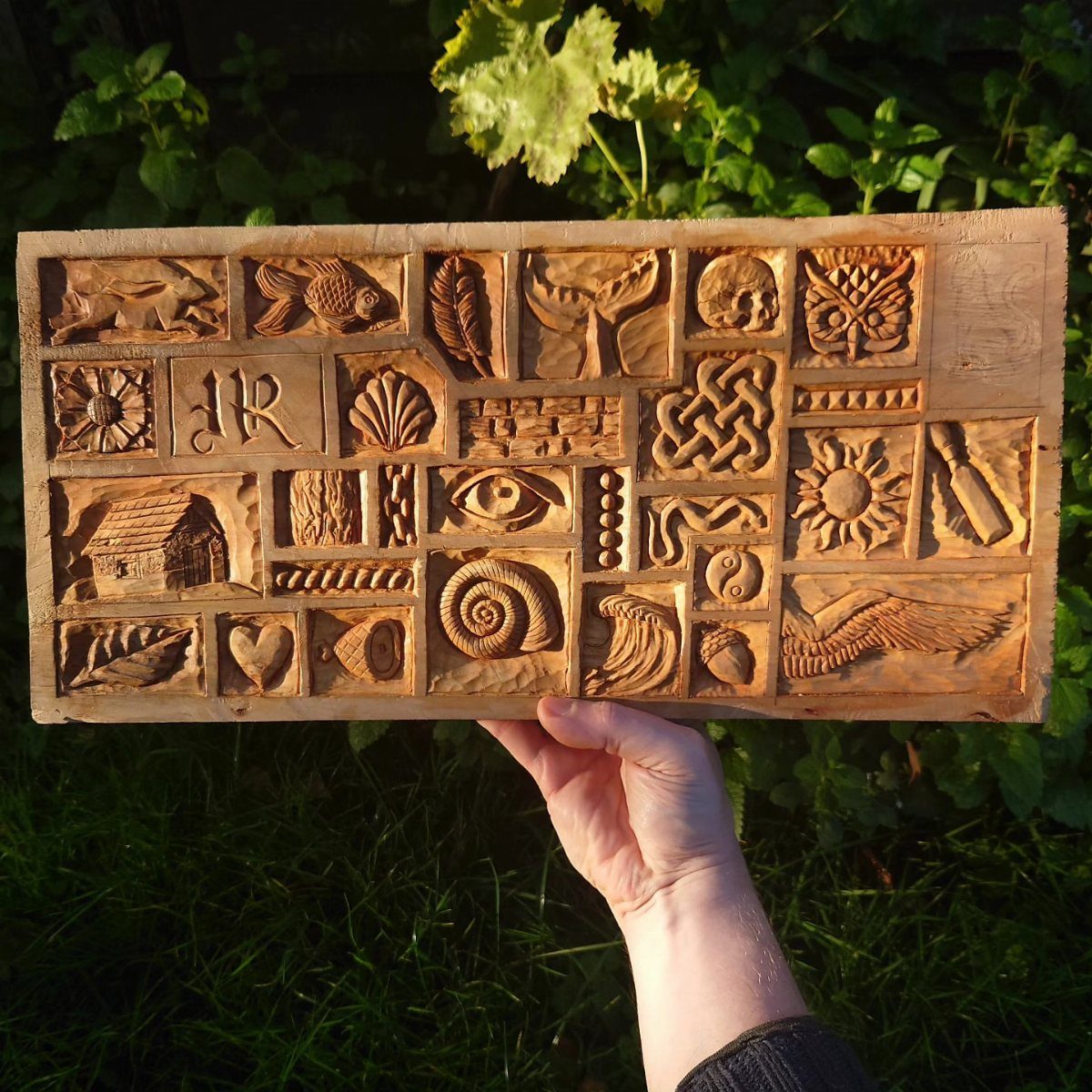 Relief Wood Carving Ideas: 5 Projects to Try at Home 3 Wooden plank with various relief carvings held up against a green garden background.