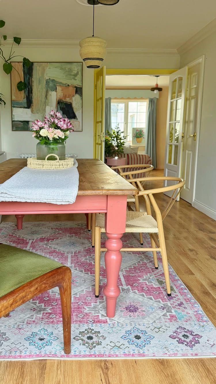 Wooden dining table with pink painted legs on a colorful patterned rug.