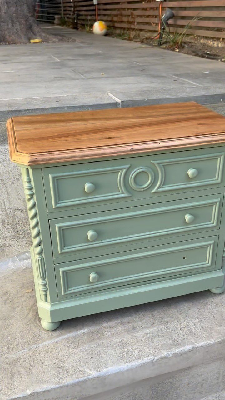 Sage green painted dresser with a natural wood top on a concrete patio.