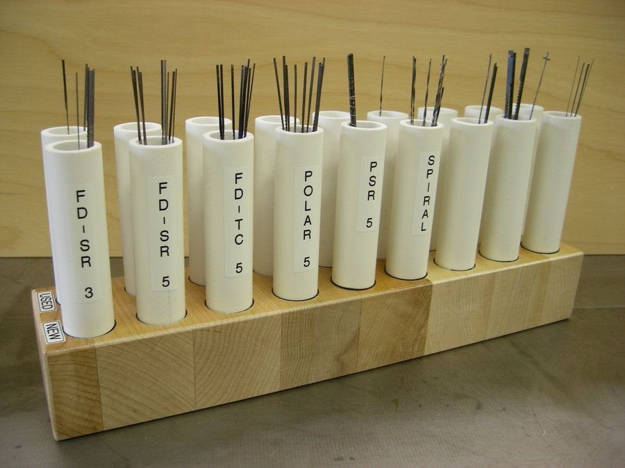 White plastic storage tubes holding scroll saw blades in a wooden base.