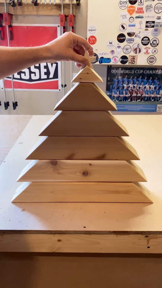 Wooden Christmas tree made of stacked planks with a hand adding a star topper.