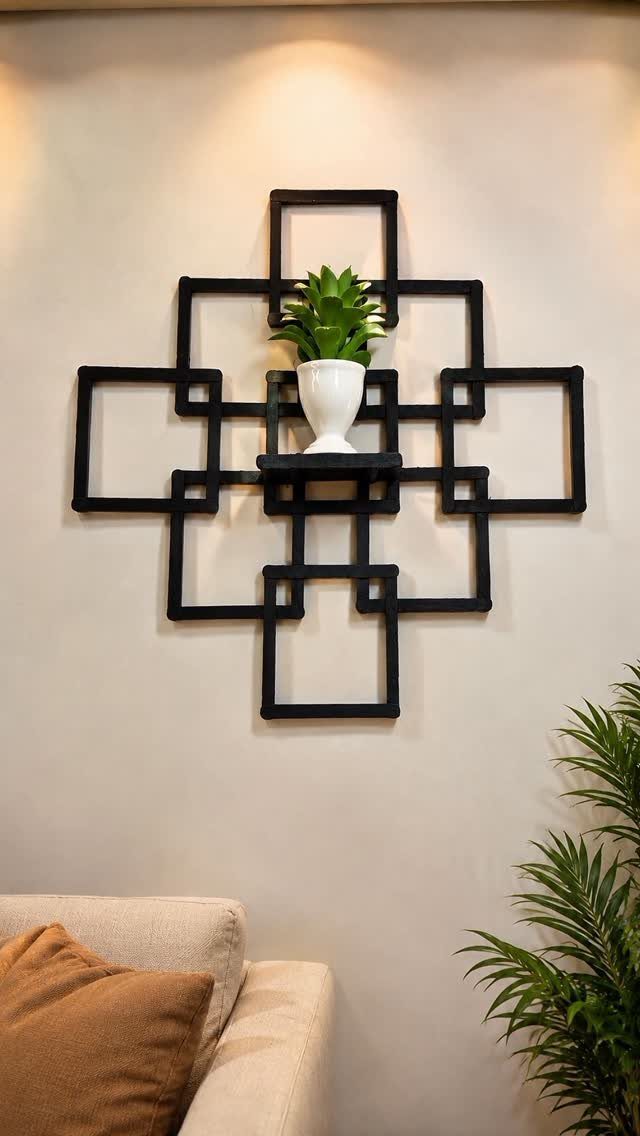 Geometric black wood wall art with a small potted plant on a shelf.