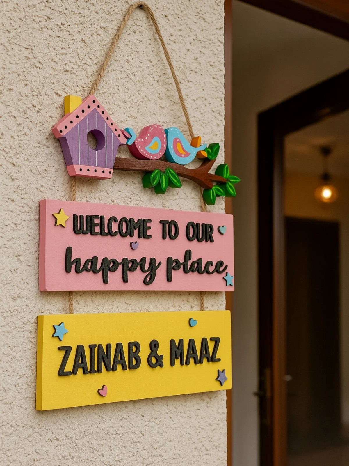 Colorful wooden hanging plaque with a birdhouse and the names Zainab and Maaz.