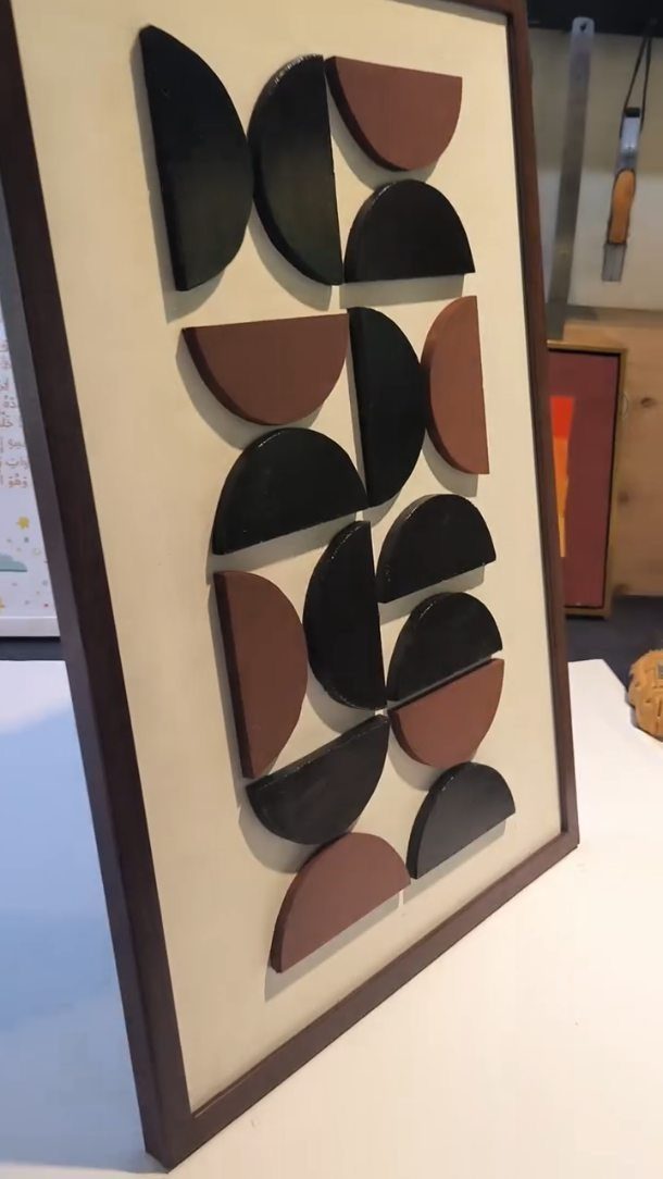 Abstract wall art with black and brown wooden semi-circles on a beige background.
