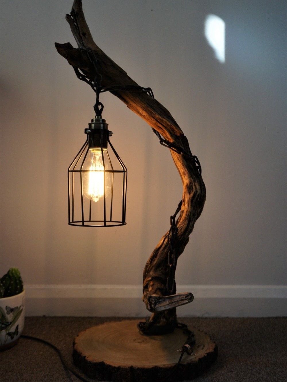 Rustic driftwood lamp with a hanging black metal cage lantern and glowing bulb.