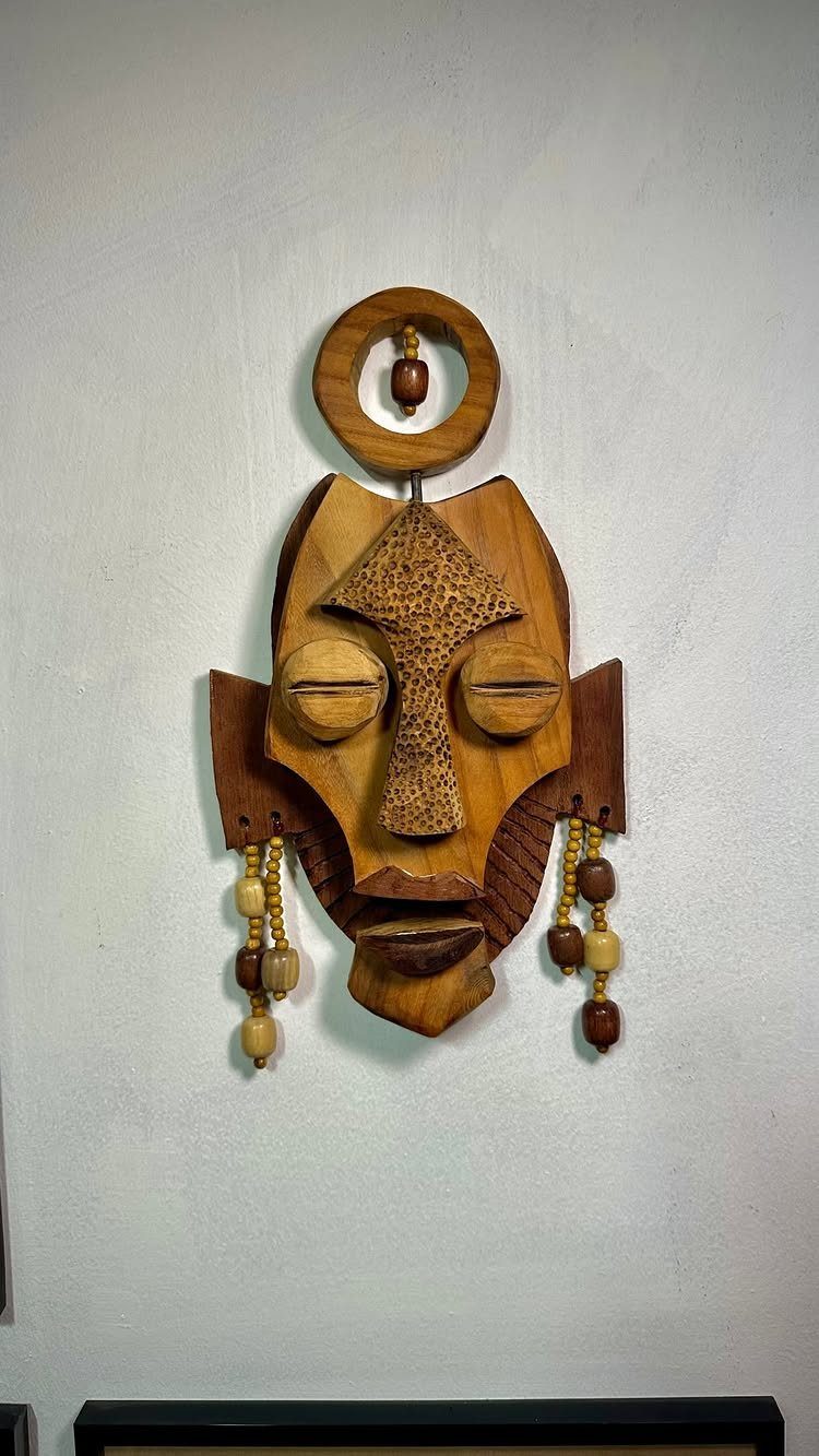 Wooden mask art piece with beads and a ring on a white wall