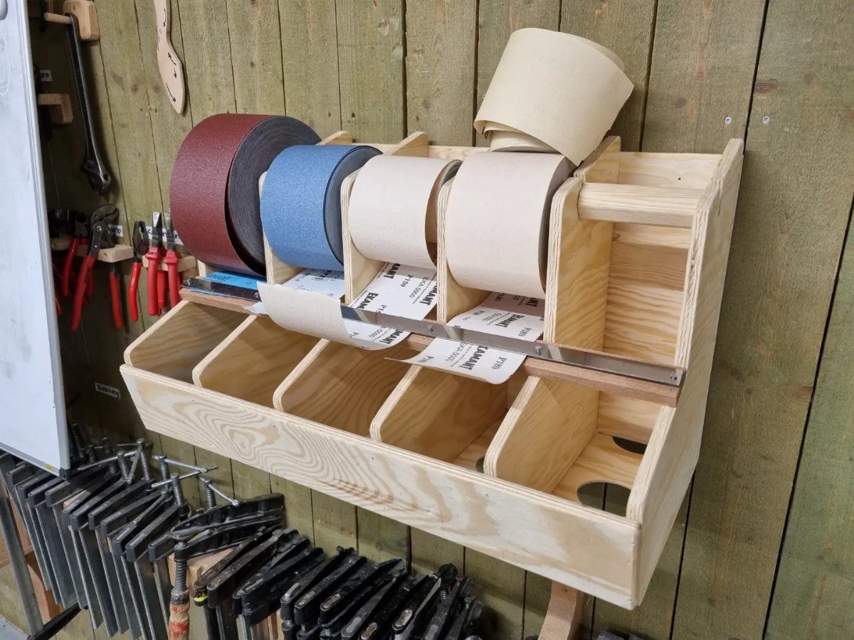 14 Shop Class Projects to Build: Bookshelf to Plywood Cart 13 Wooden sandpaper organizer holding colorful sanding rolls mounted on a green workshop wall