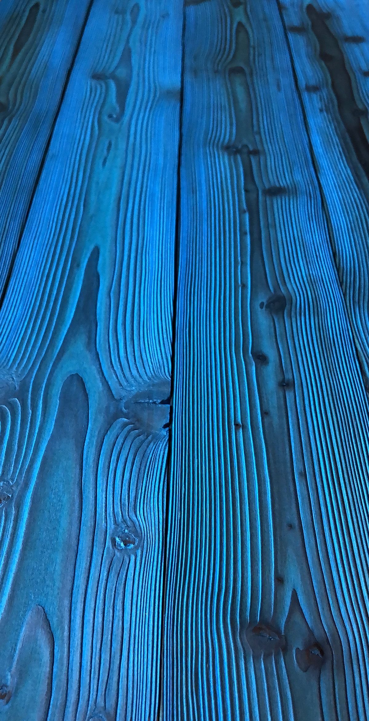 Blue stained wooden planks with charred grain patterns and deep linear textures.