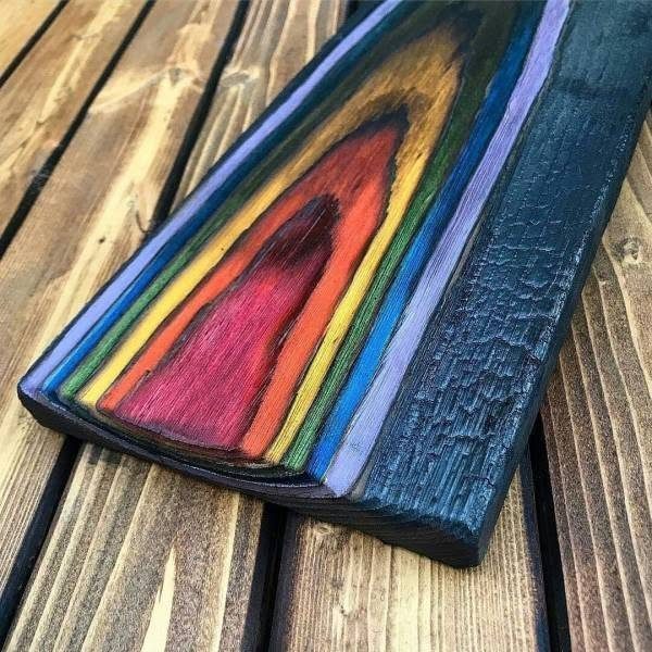Charred wood plank with vibrant rainbow colored stains resting on a wooden deck.