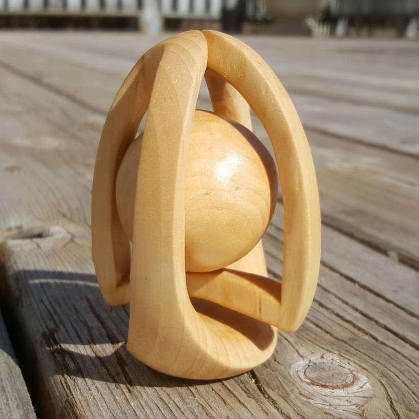 Wooden ball-in-a-cage sculpture resting on a rustic outdoor wooden deck surface