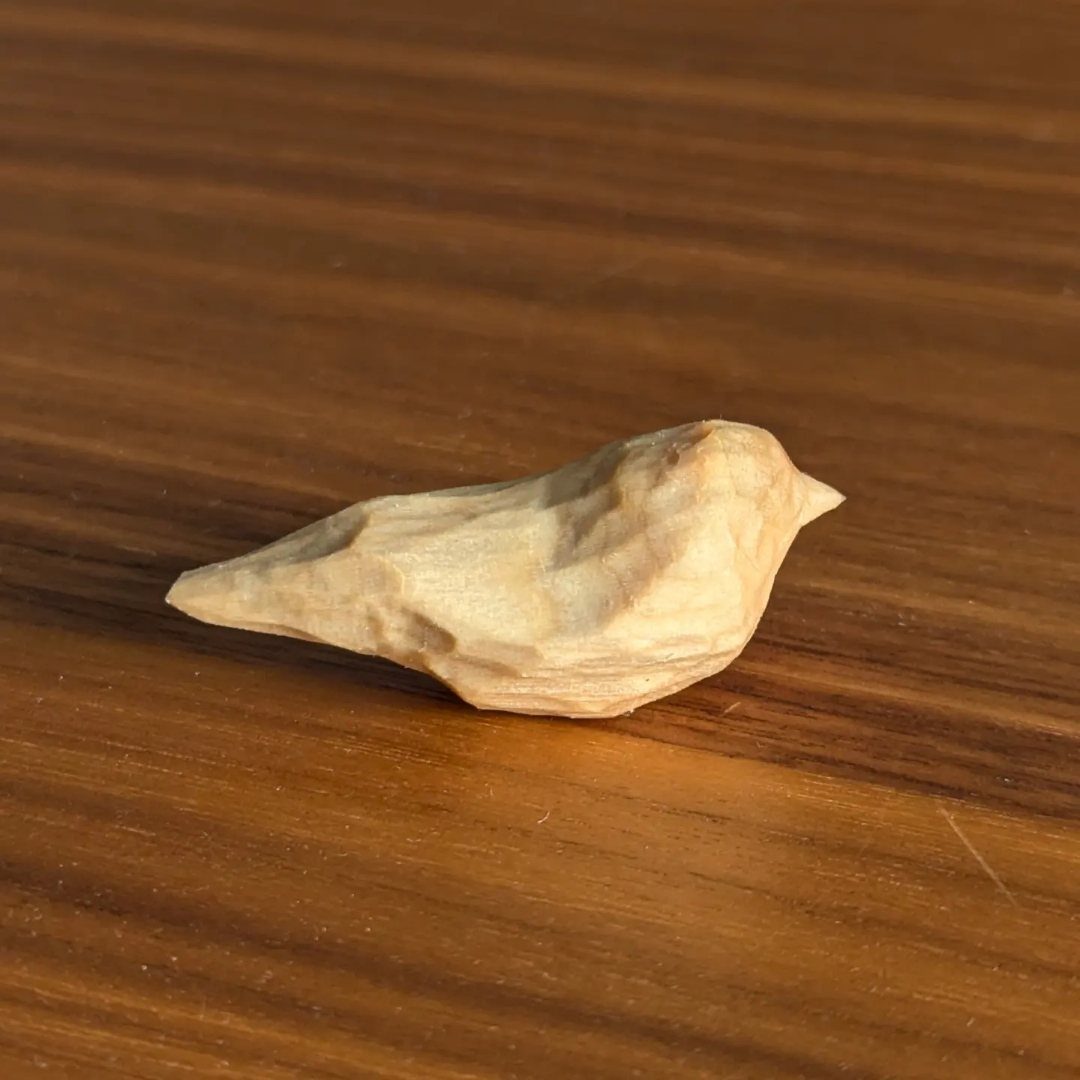 Small hand-carved wooden bird figurine resting on a polished brown wooden table.