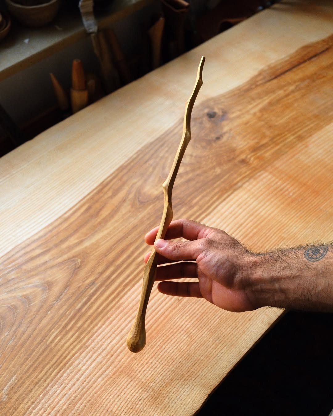 Carved organic wooden wand held by a hand over a wooden table.