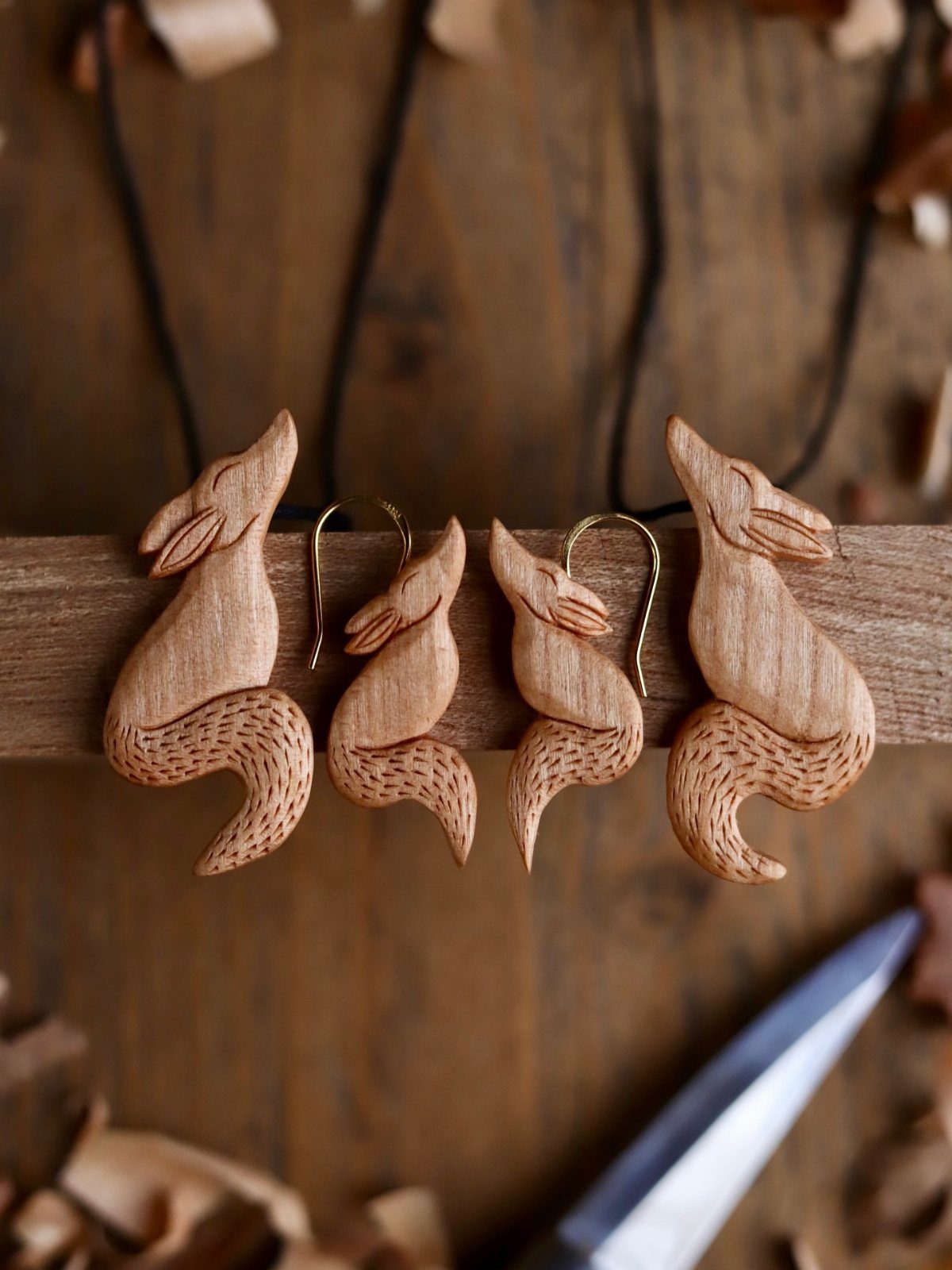Four small wooden fox carvings resting on a beam with a carving knife.