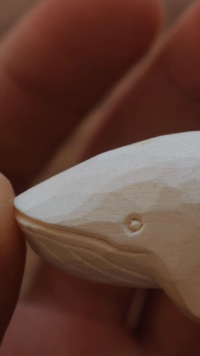 Hand-carved wooden whale with visible tool marks held between fingers.