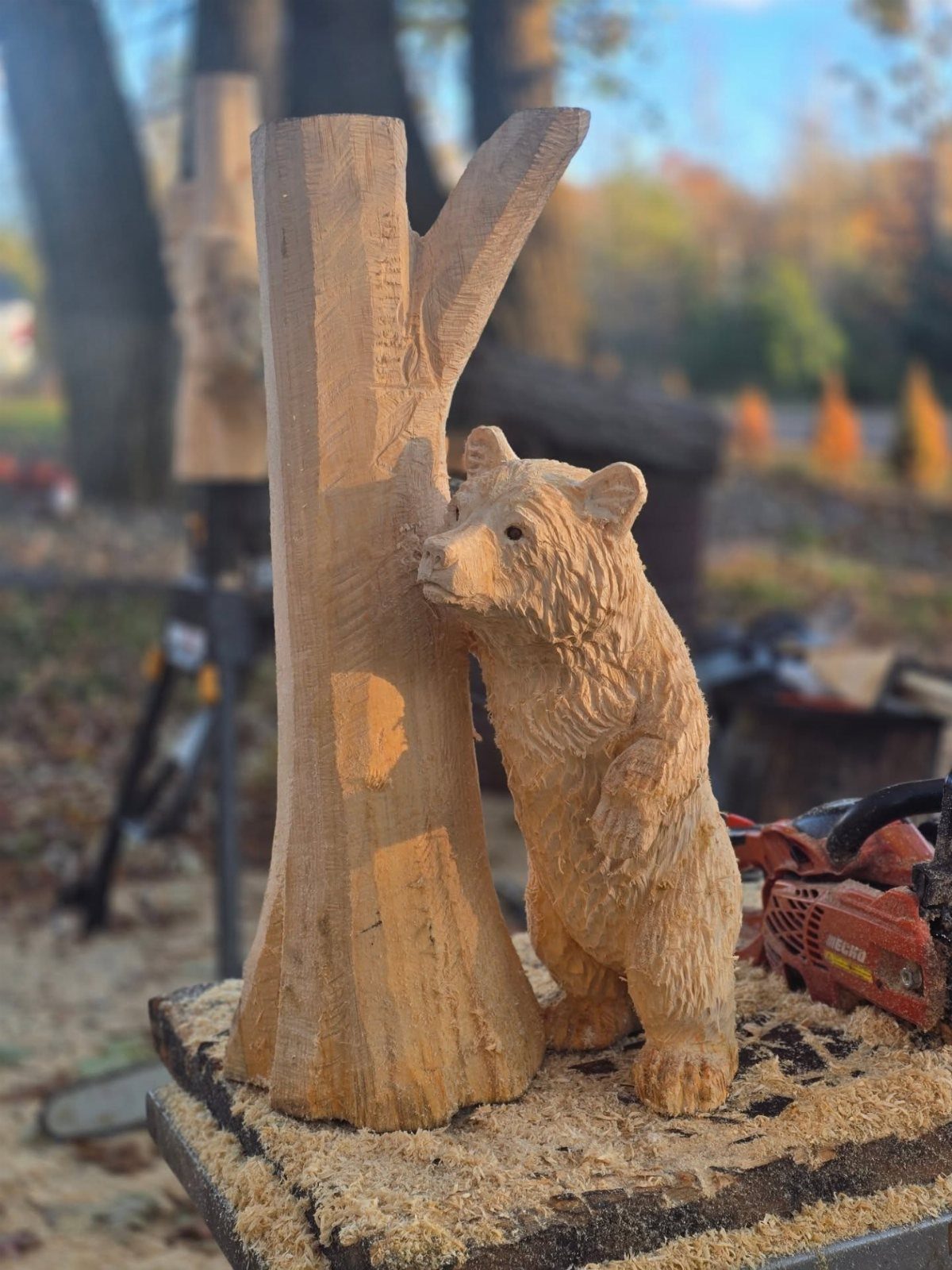 Small wooden bear carving standing beside a carved tree trunk on sawdust.