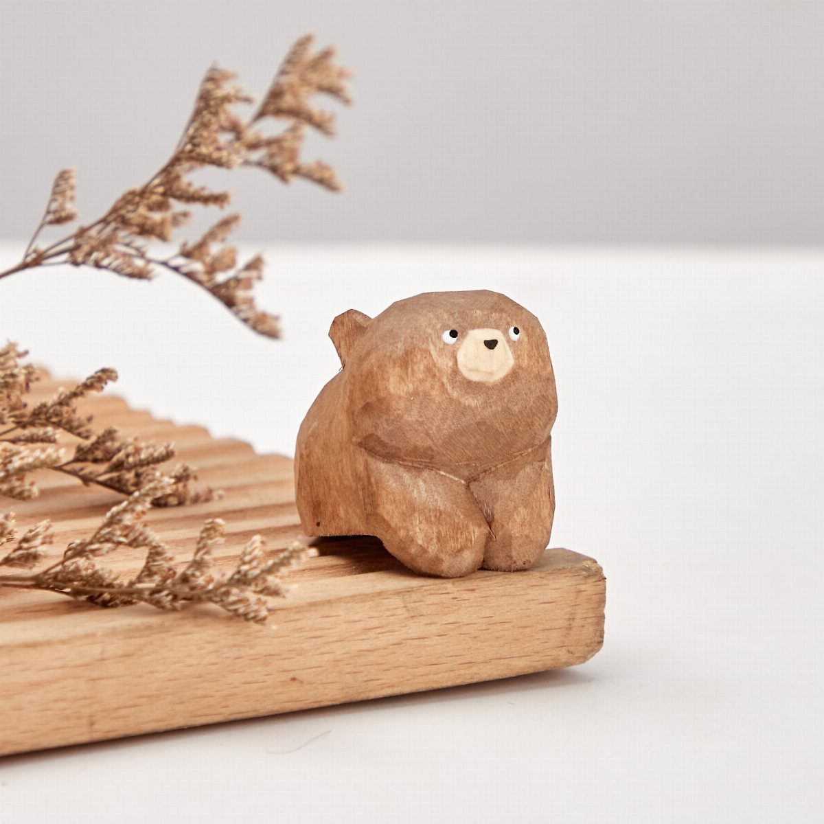 Small hand-carved wooden bear figurine sitting on a light wood slatted surface.