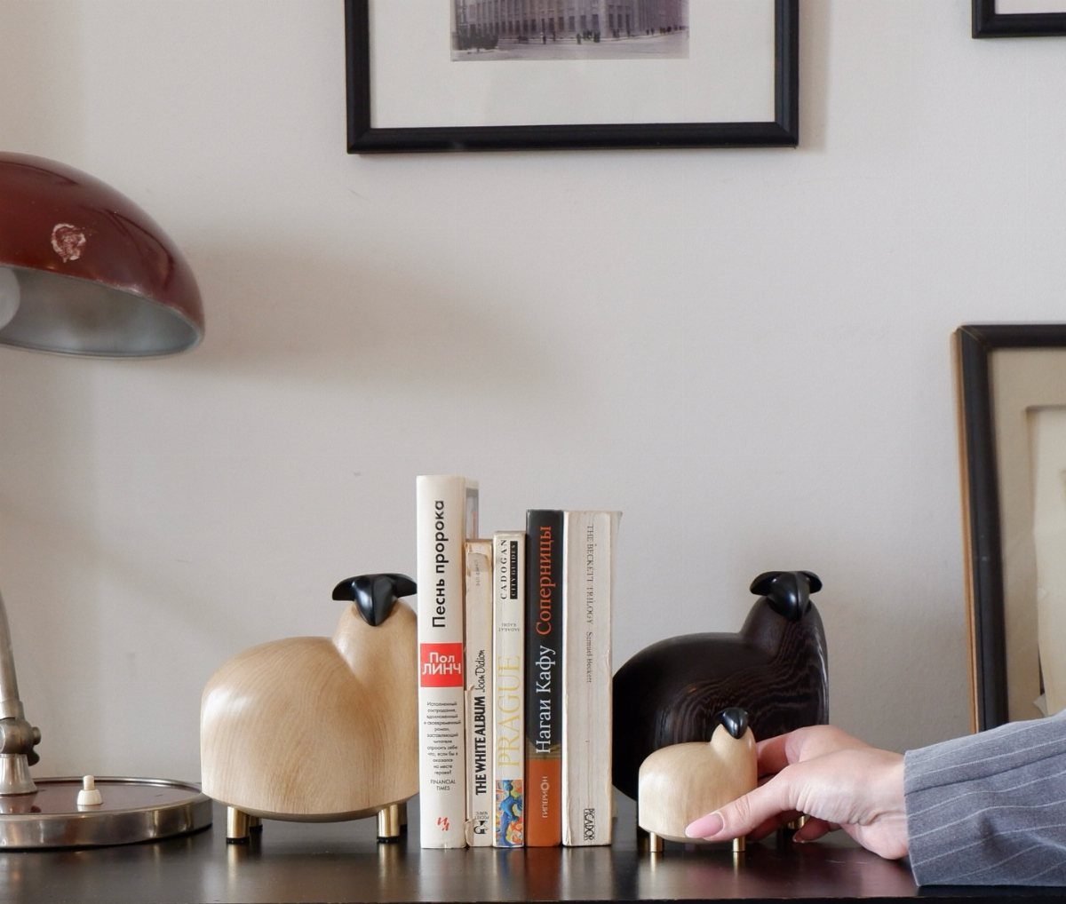 Three carved wooden sheep figurines standing on a desk next to books.