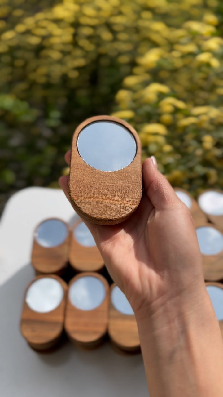 Small oval wooden mirrors held in a hand with others on a white table