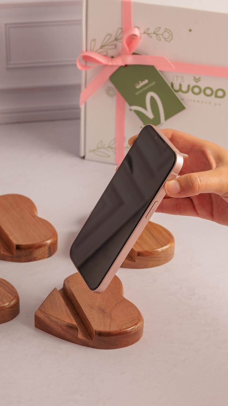 Heart-shaped wooden phone stands on a white surface with a gift box background.