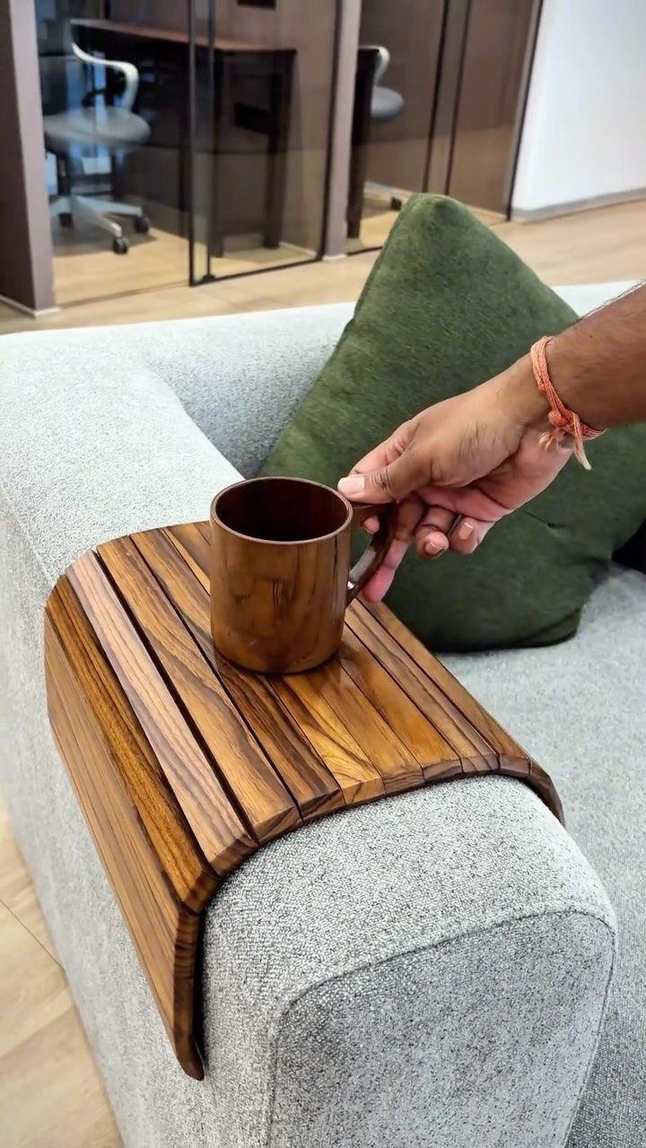 Wooden sofa arm rest tray holding a brown mug on a grey couch.