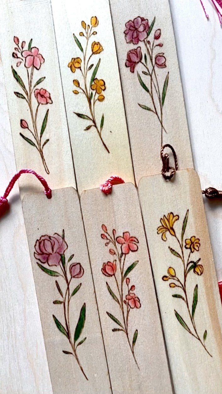 Wooden bookmarks with painted pink and yellow flowers and red string ties.