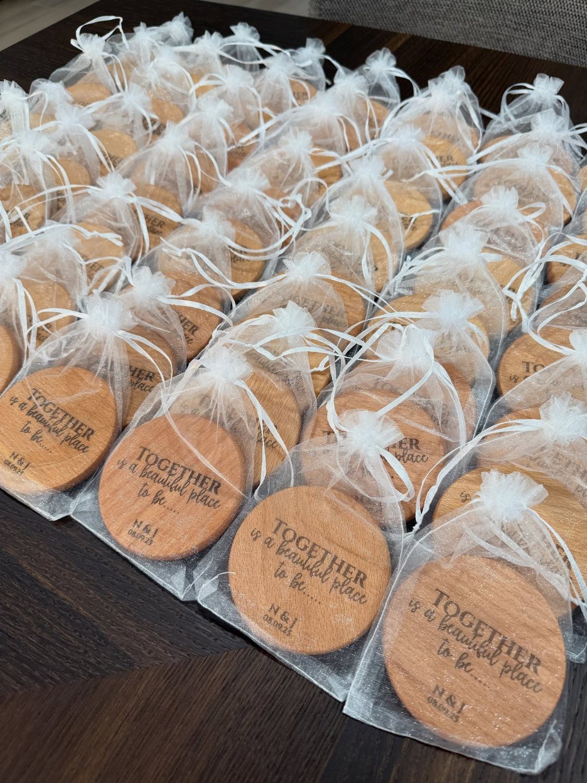 Round wooden coasters with engraved text inside white organza drawstring gift bags.