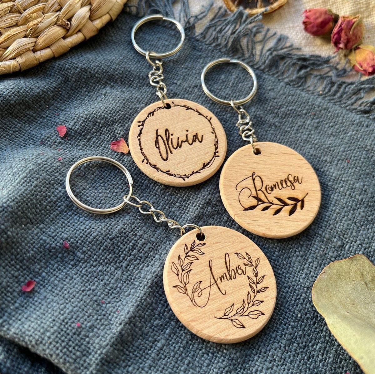 Three circular wooden keychains with engraved names resting on a blue fabric background.