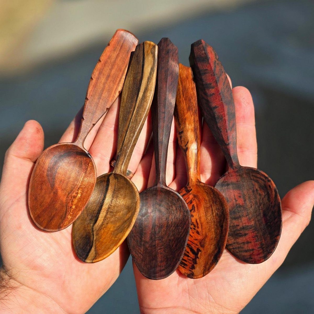 Five hand-carved wooden spoons of different grains held in an open palm.