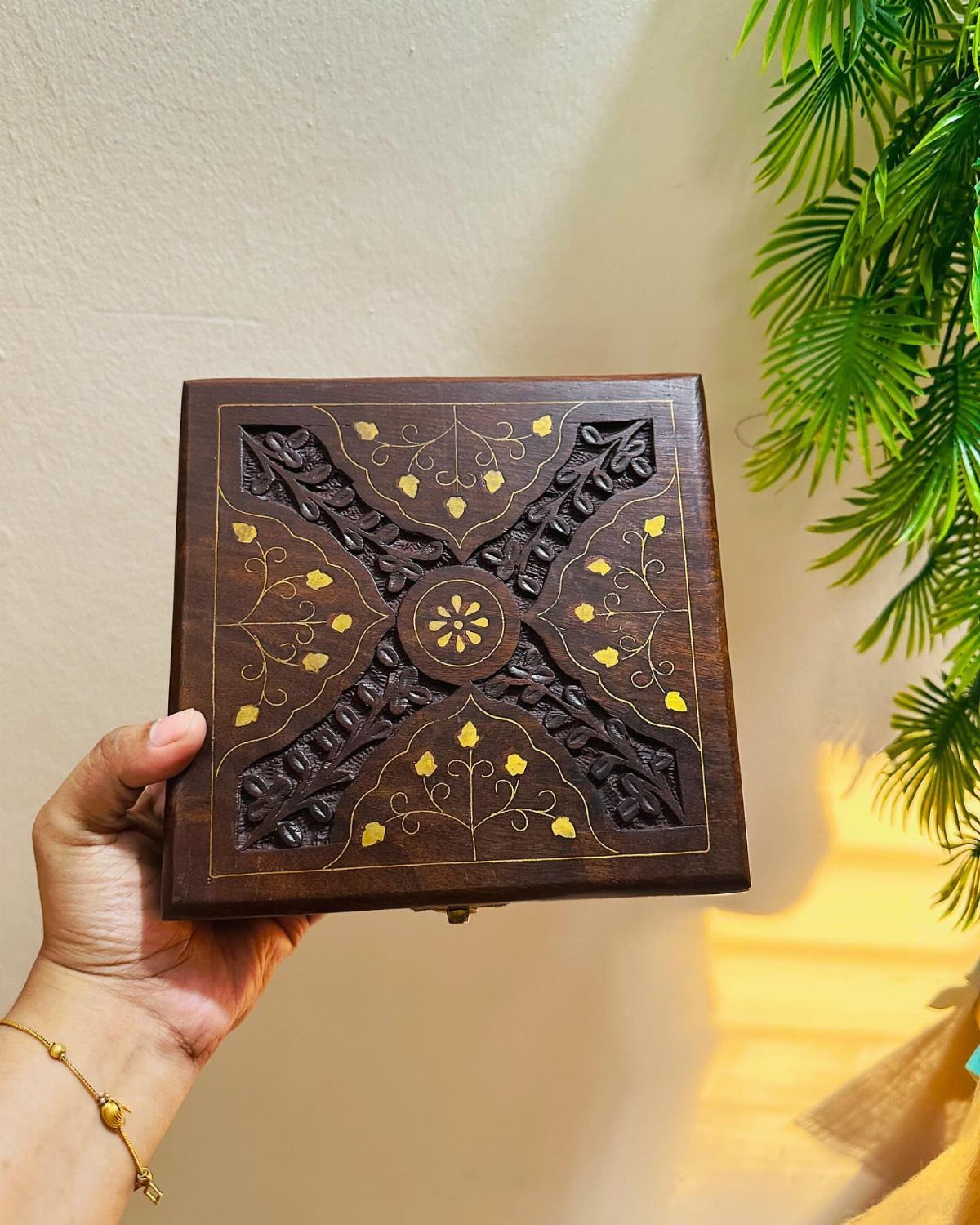 Carved dark brown wooden jewelry box with gold accents held by a hand.