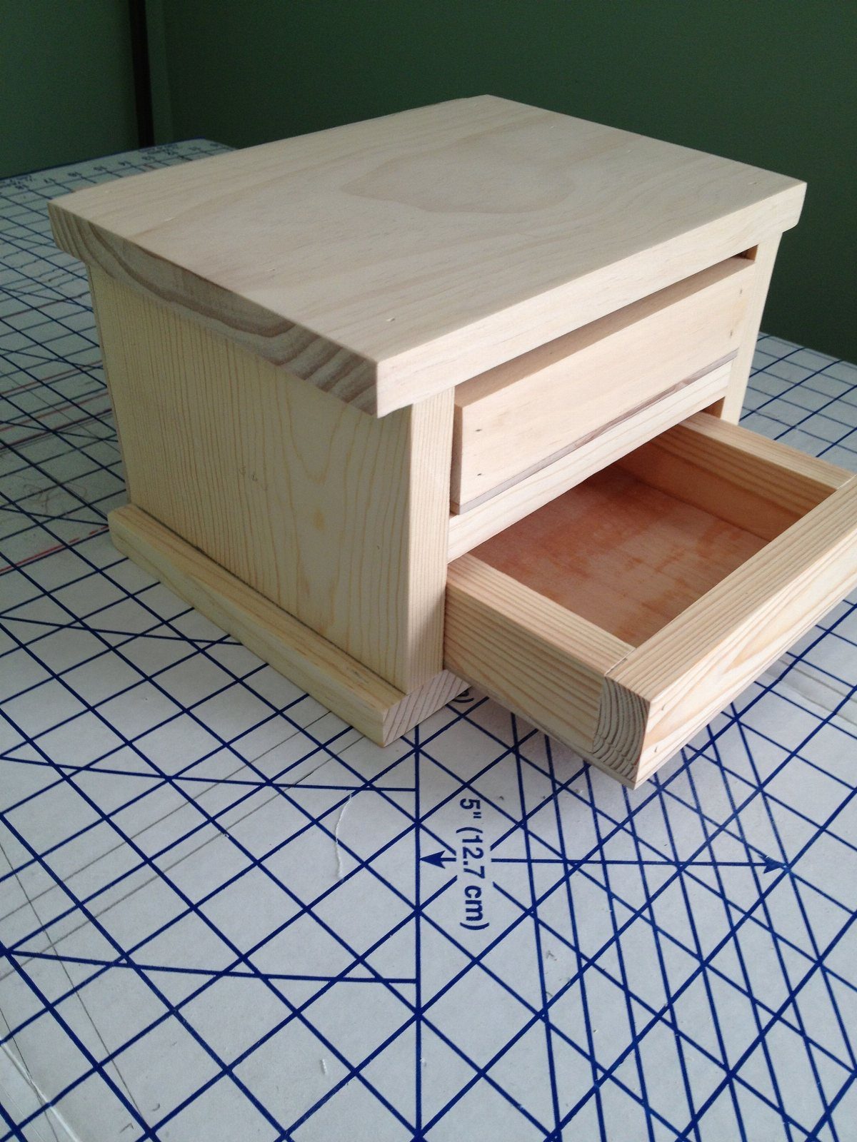 Small light wood jewelry box with two drawers on a blue grid mat.