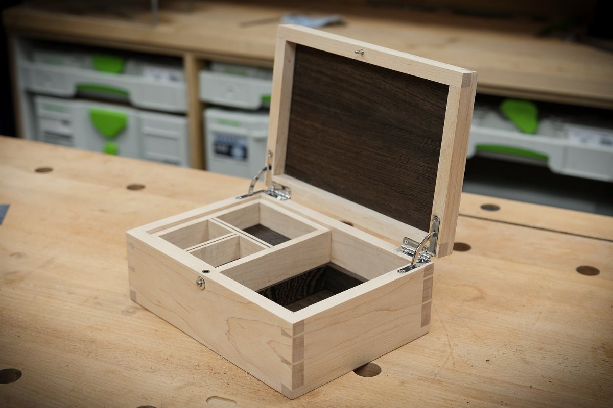 Open light wood jewelry box with interior compartments on a wooden workbench