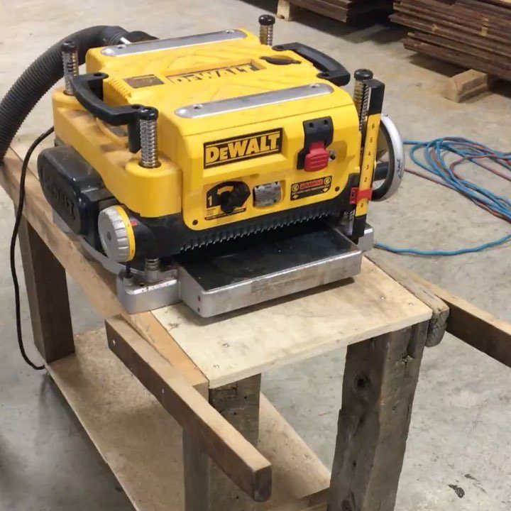 Yellow DeWalt thickness planer on a custom wooden workbench in a workshop.