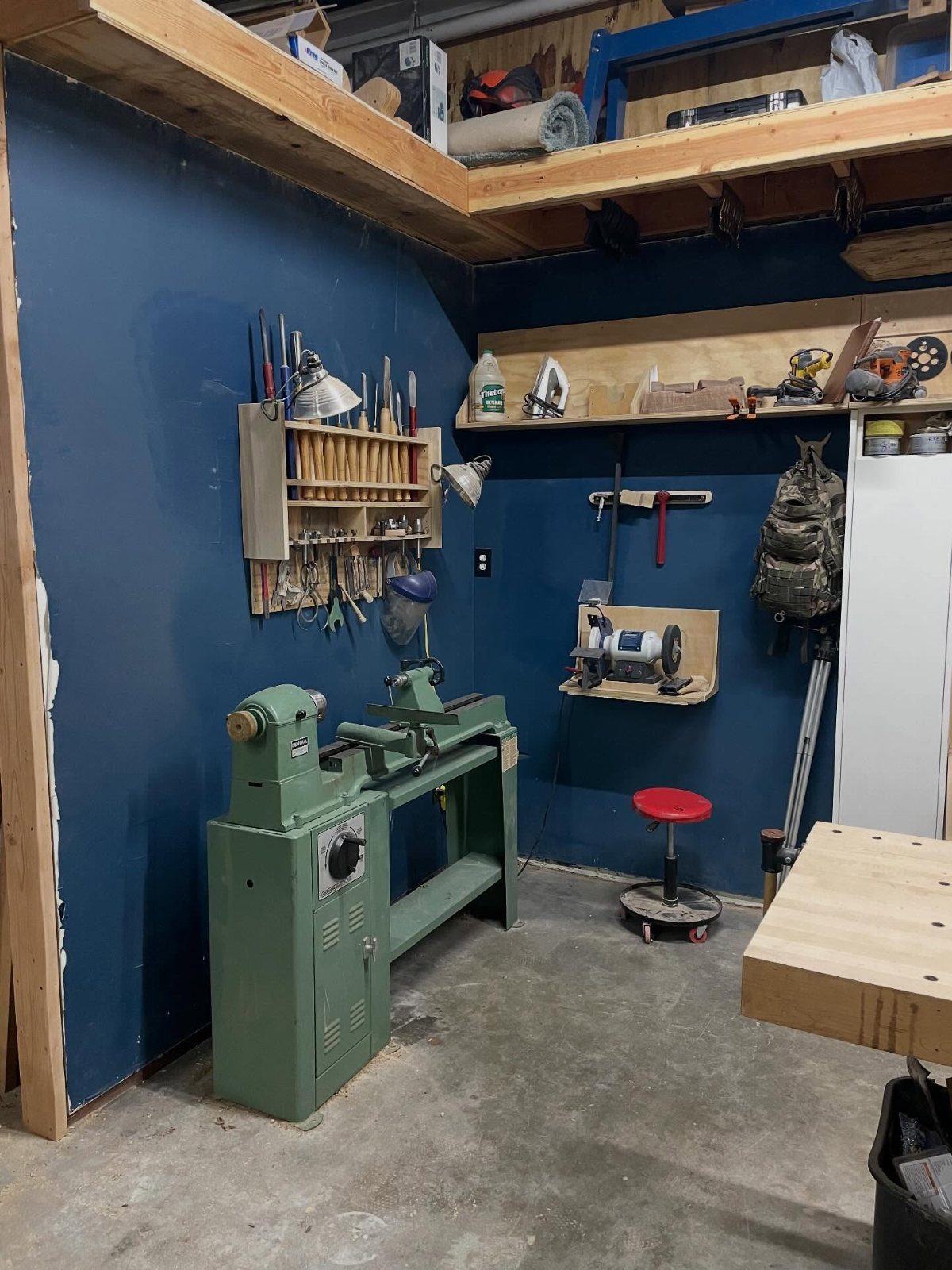 Small woodworking shop with a green lathe, tool racks, and blue walls.