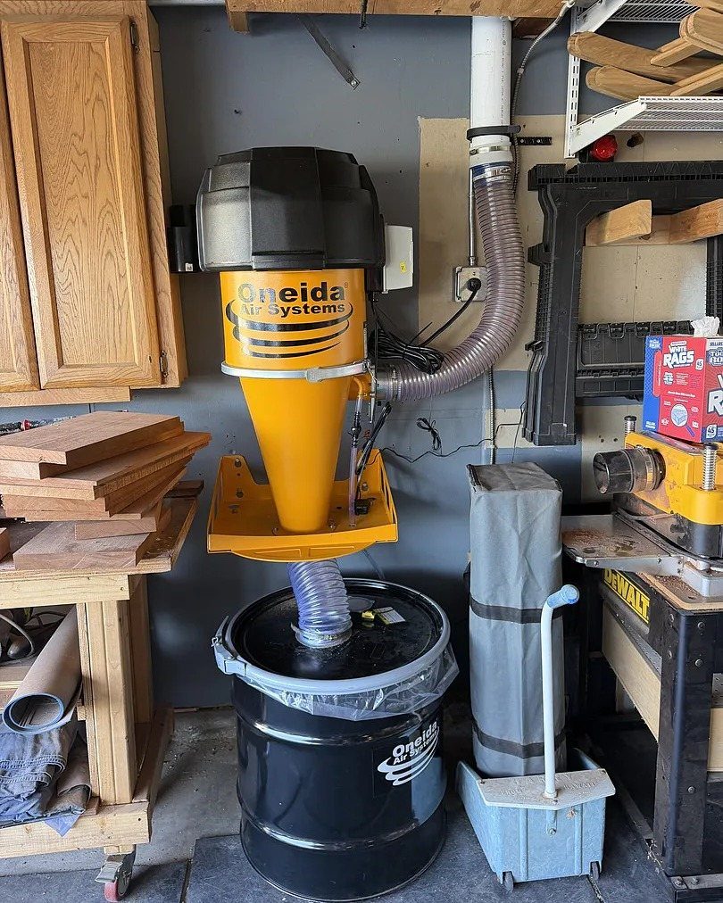 Yellow Oneida dust collector system with a black collection drum in a woodshop.