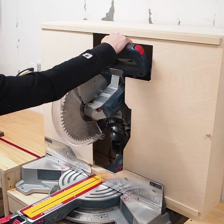 Miter saw integrated into a custom light wood cabinet workstation in a workshop.