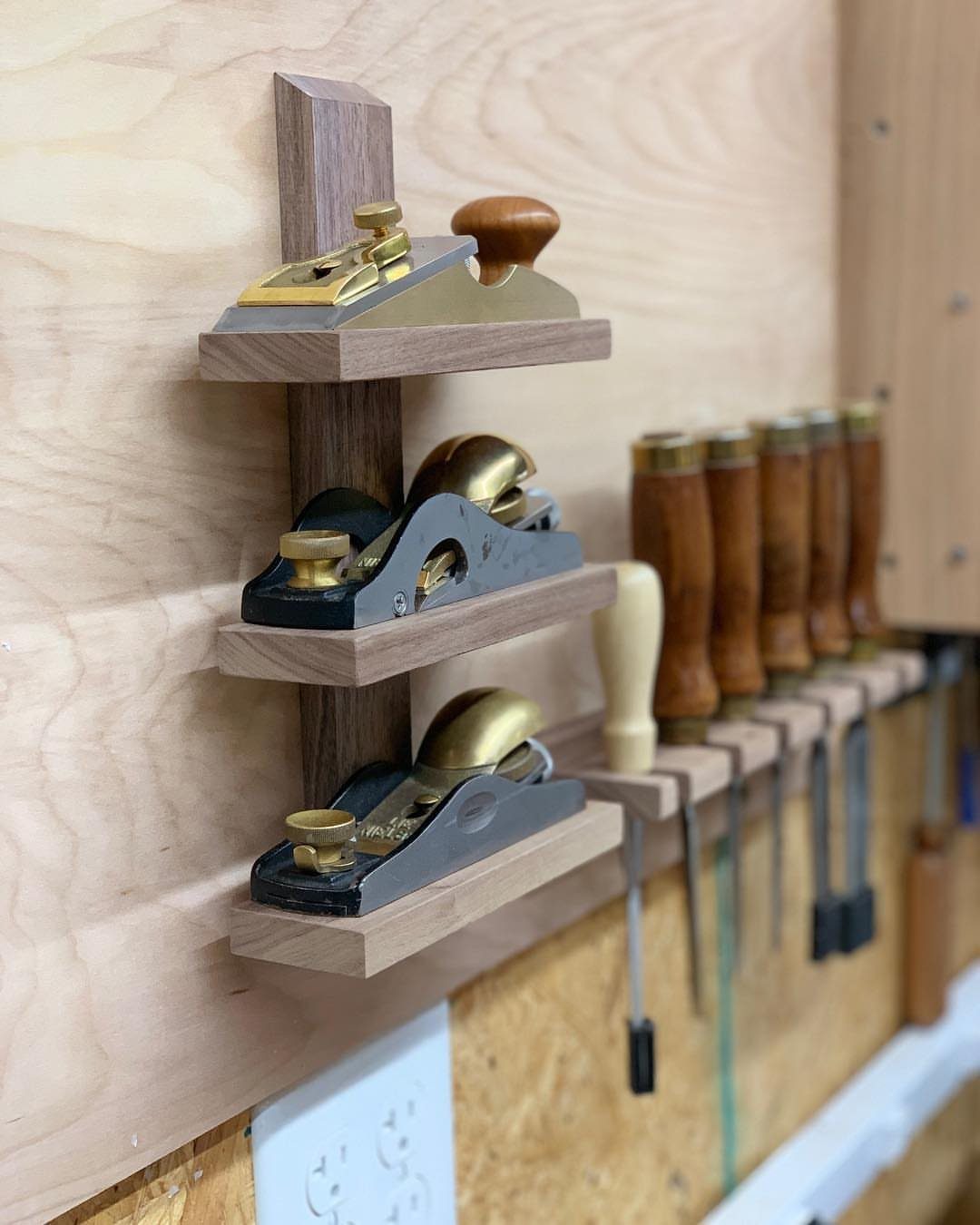 Hand planes and chisels organized on wooden wall racks in a woodworking shop.