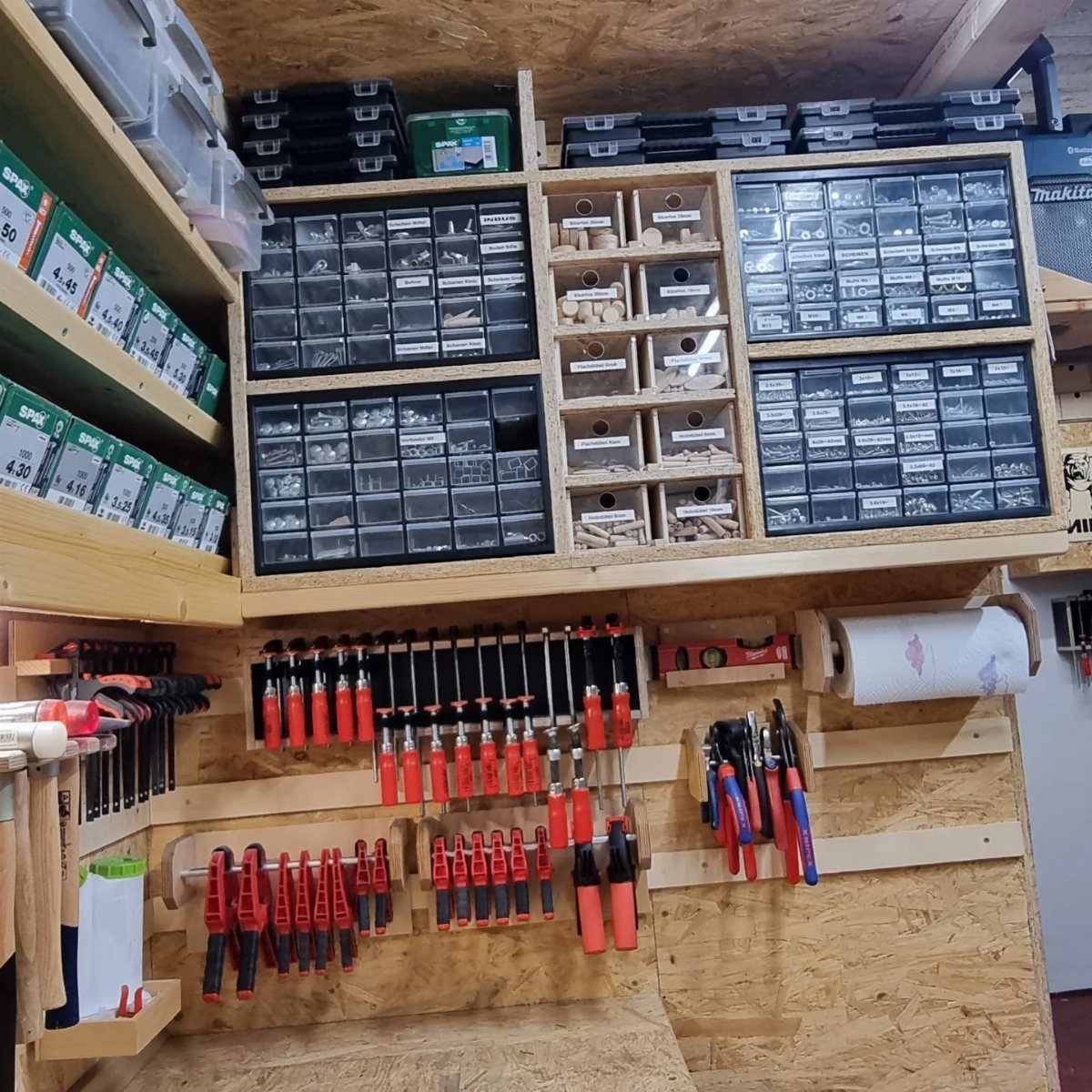 Organized woodshop wall with hardware drawers and red clamps on a wooden rack