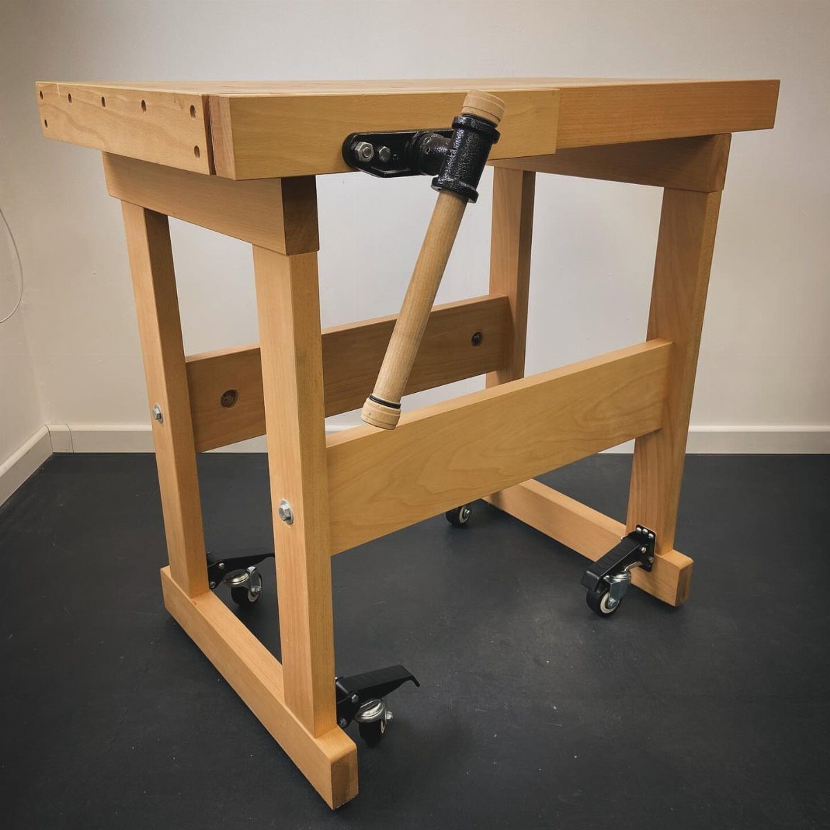 Small Woodworking Bench Ideas: 5 Designs for Tight Spaces 2 Small wooden woodworking bench with a vice and caster wheels on a dark floor.