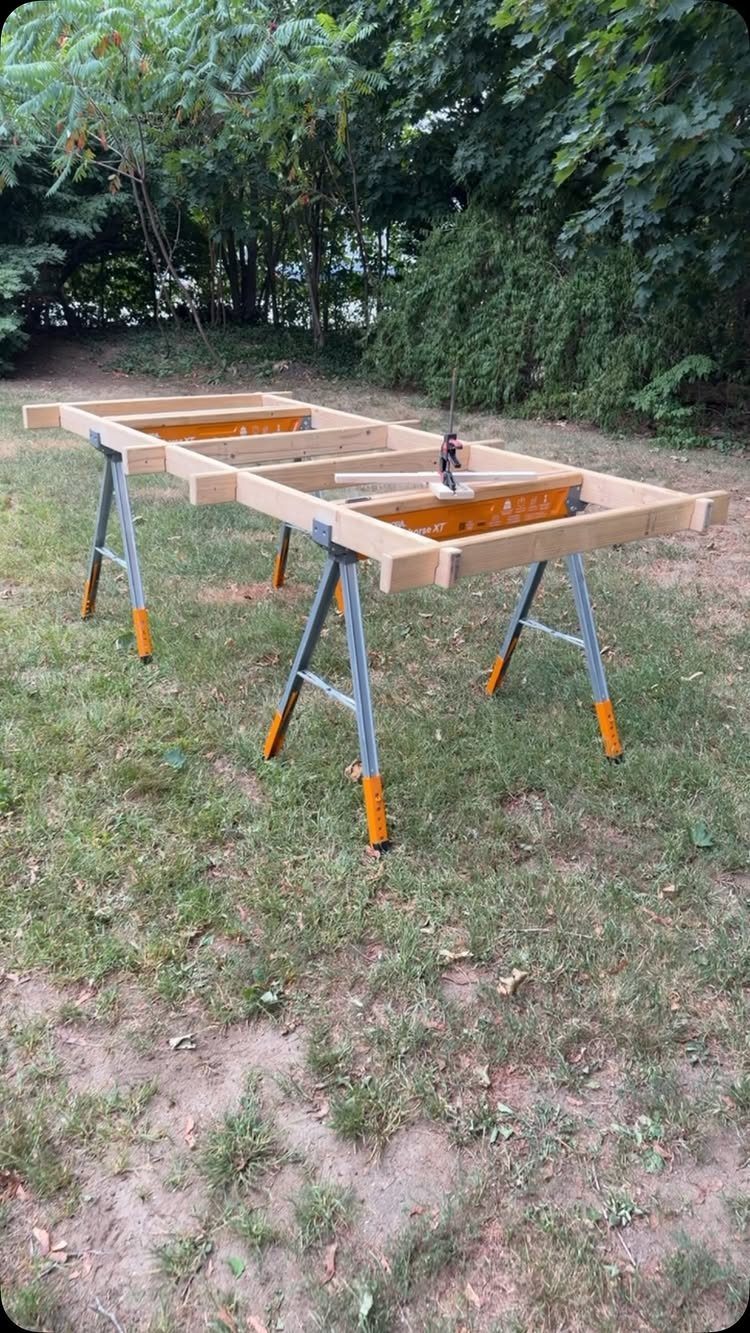 Small Woodworking Bench Ideas: 5 Designs for Tight Spaces 5 Small wooden workbench frame supported by two orange and grey folding sawhorses outdoors.