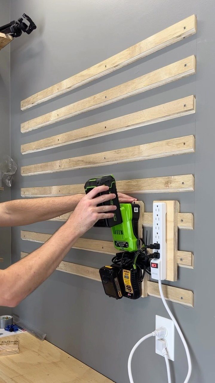 Person placing a battery on a charger mounted to a wooden slat wall.