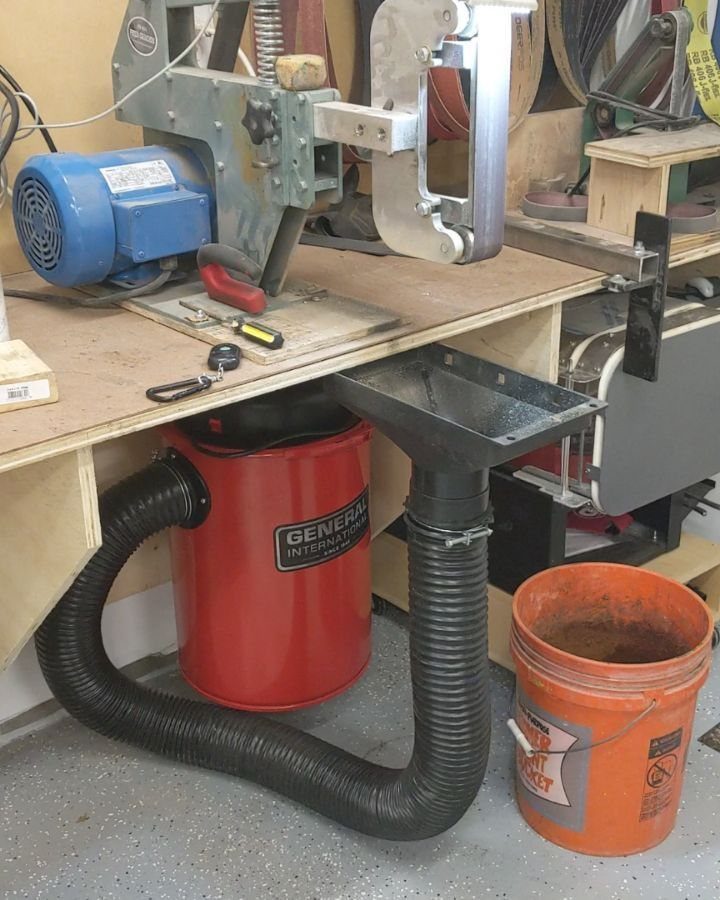 Red vacuum canister with black hose and metal funnel under a wooden workbench.