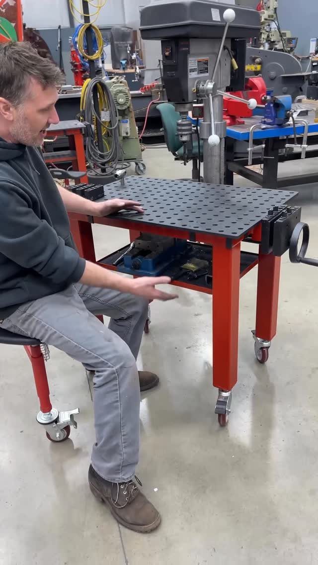 Red mobile workbench with caster wheels and a man sitting in a workshop.