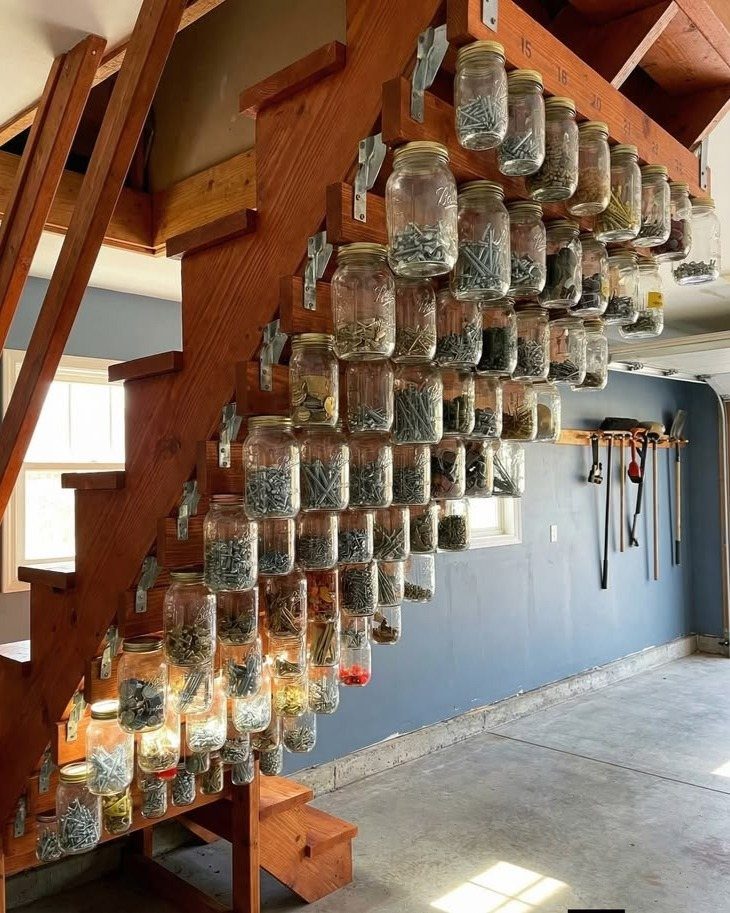 Glass jars of hardware mounted under wooden stairs in a small workshop garage.