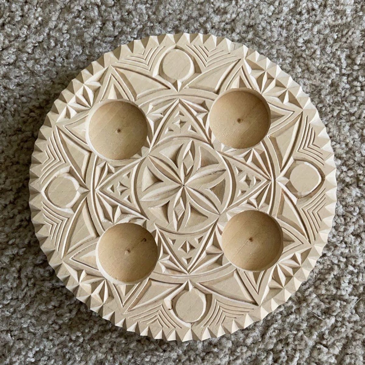 Circular wooden disc with intricate chip-carved geometric patterns and four small circular holes.