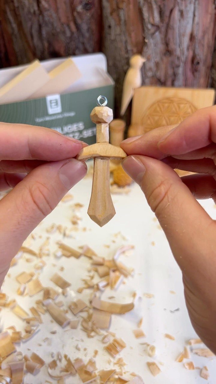 Small hand-carved wooden sword held by two hands over a pile of shavings.