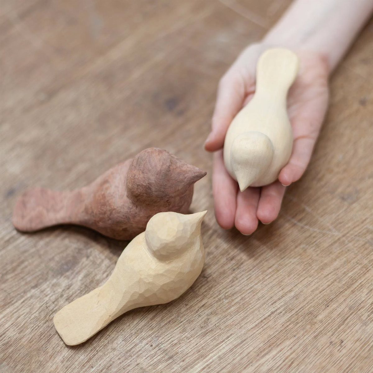 Three small hand-carved wooden birds, one resting in a person's open palm.
