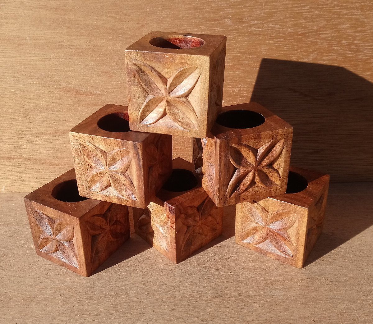 Wooden cubes with carved four-petaled flowers stacked on a light brown wooden surface.