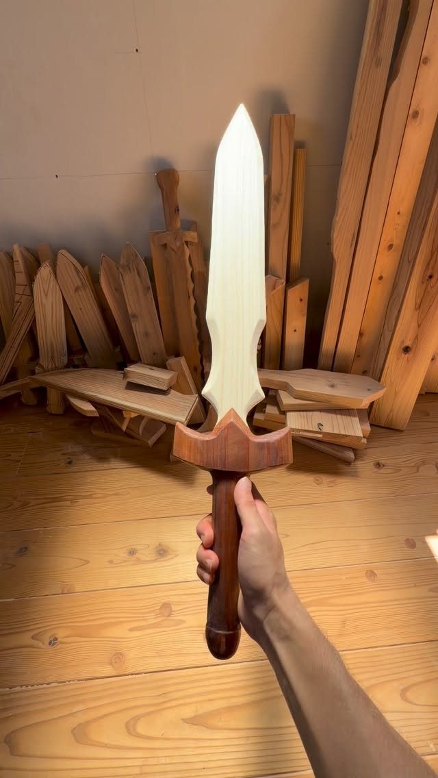 Hand holding a carved wooden toy sword with a light blade and dark hilt.