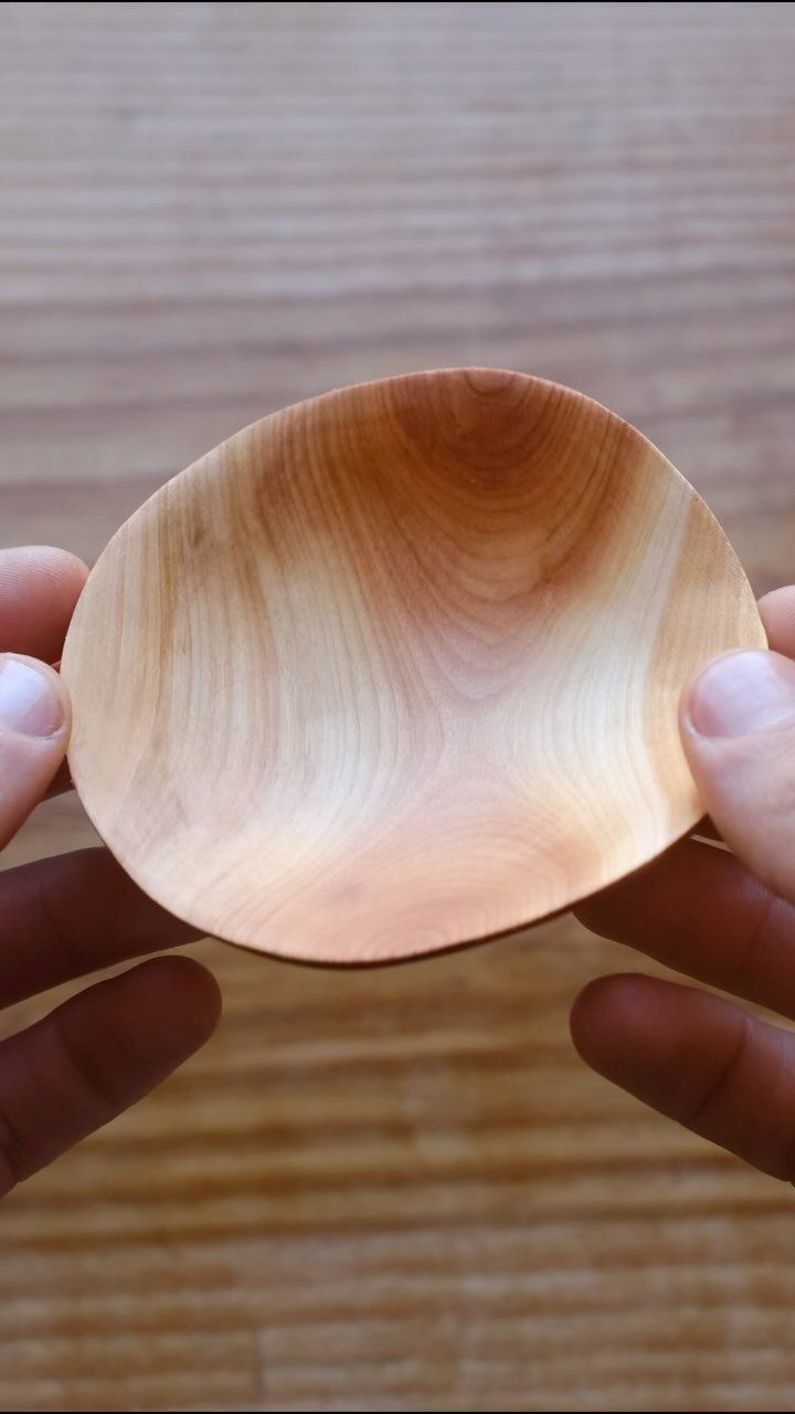 Small hand-carved wooden bowl held by two hands against a wooden background.